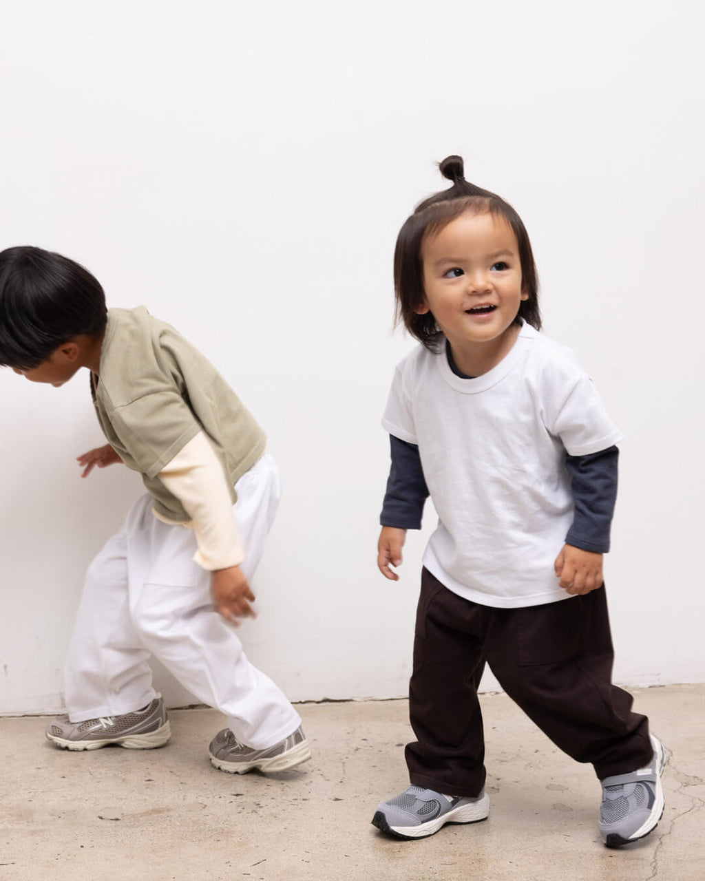 Two kids standing by a wall laughing and playing in LESET Bebe Tshirts and Margo Pants