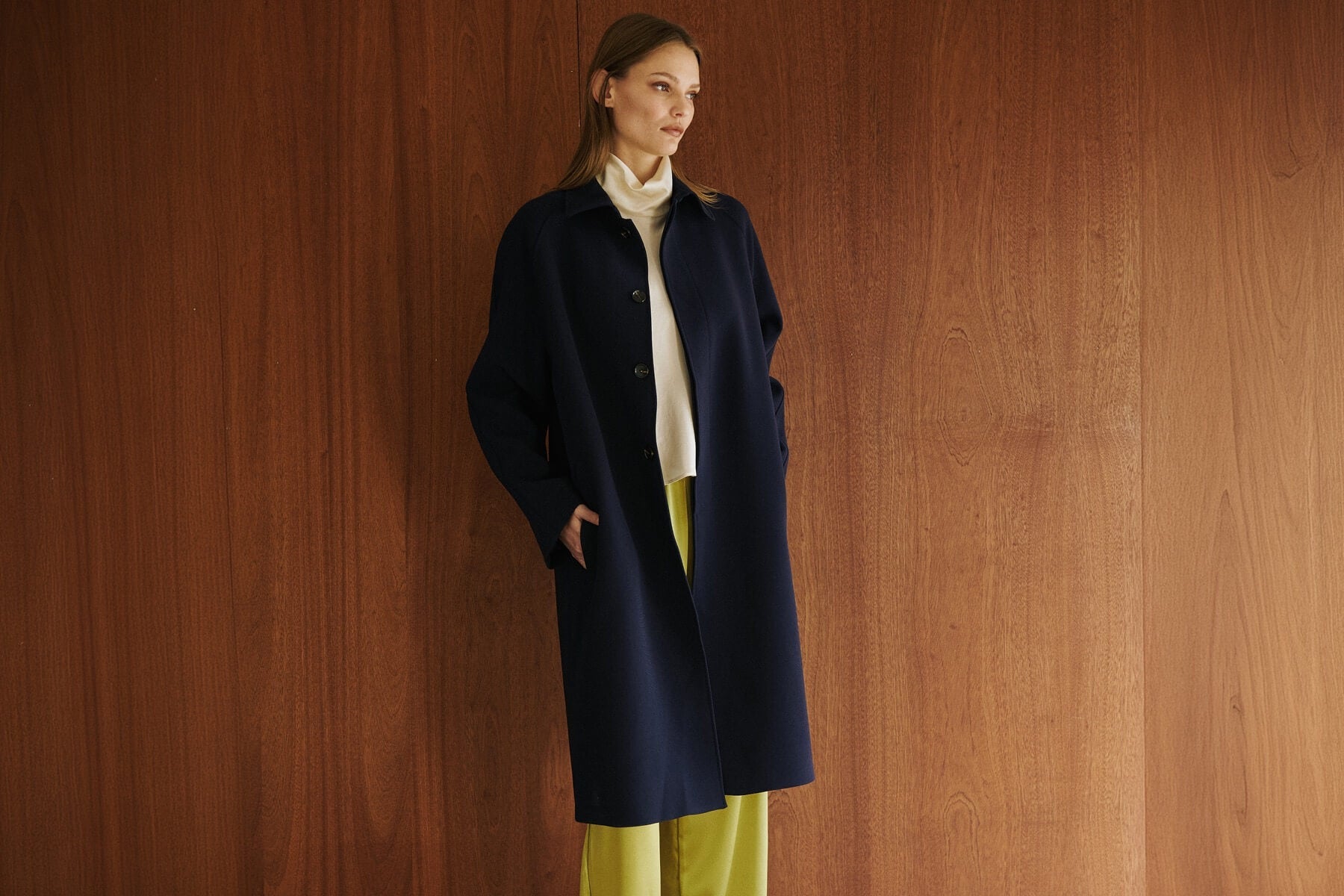 woman standing against wall in navy coat and chartreuse pants