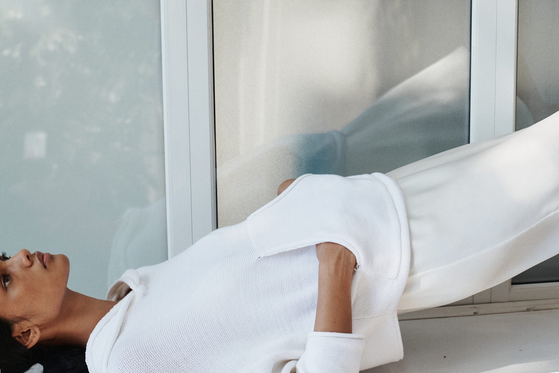 Side of woman wearing a white sweatshirt with white pants.