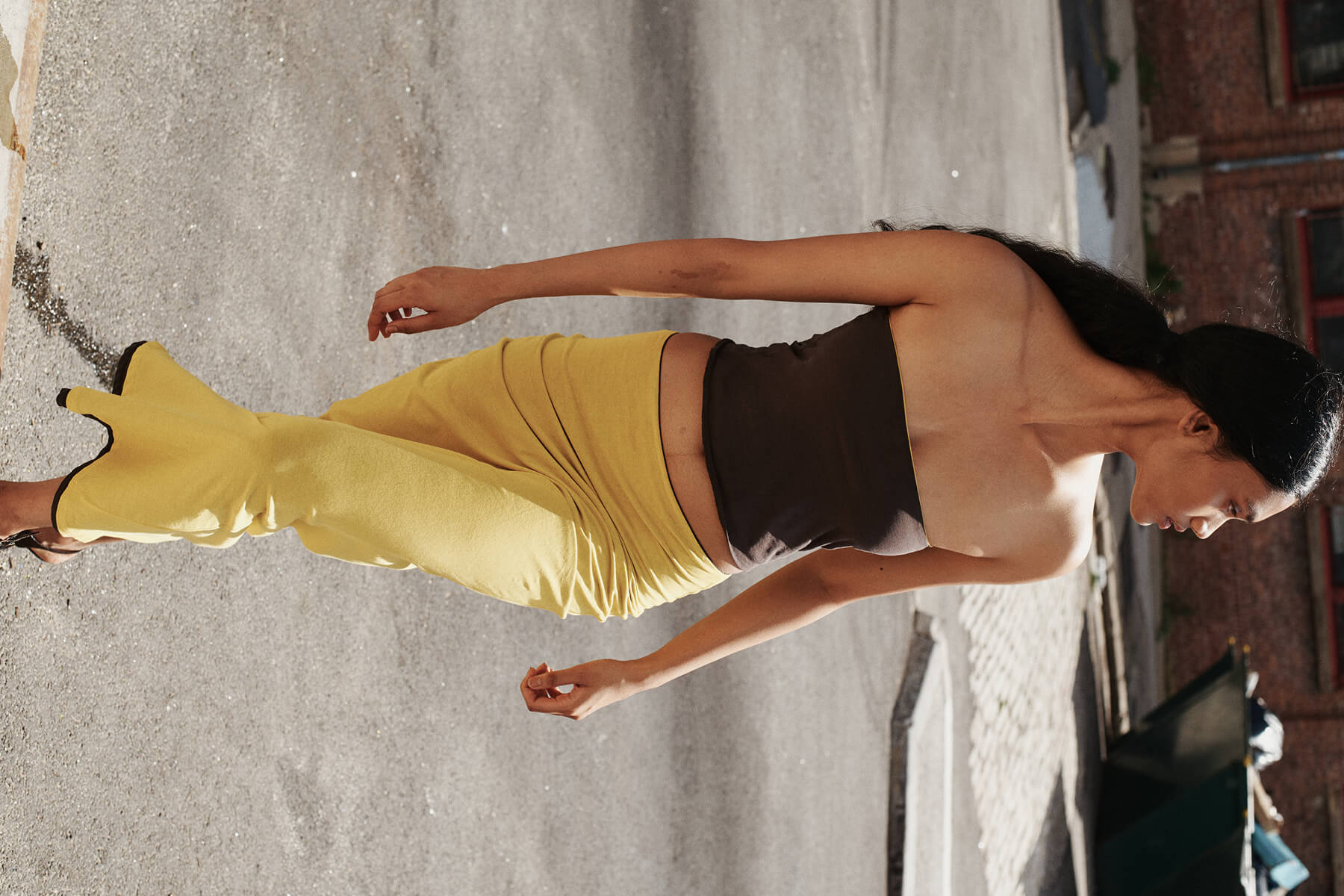 Woman walking in brown bandeau top with yellow skirt.