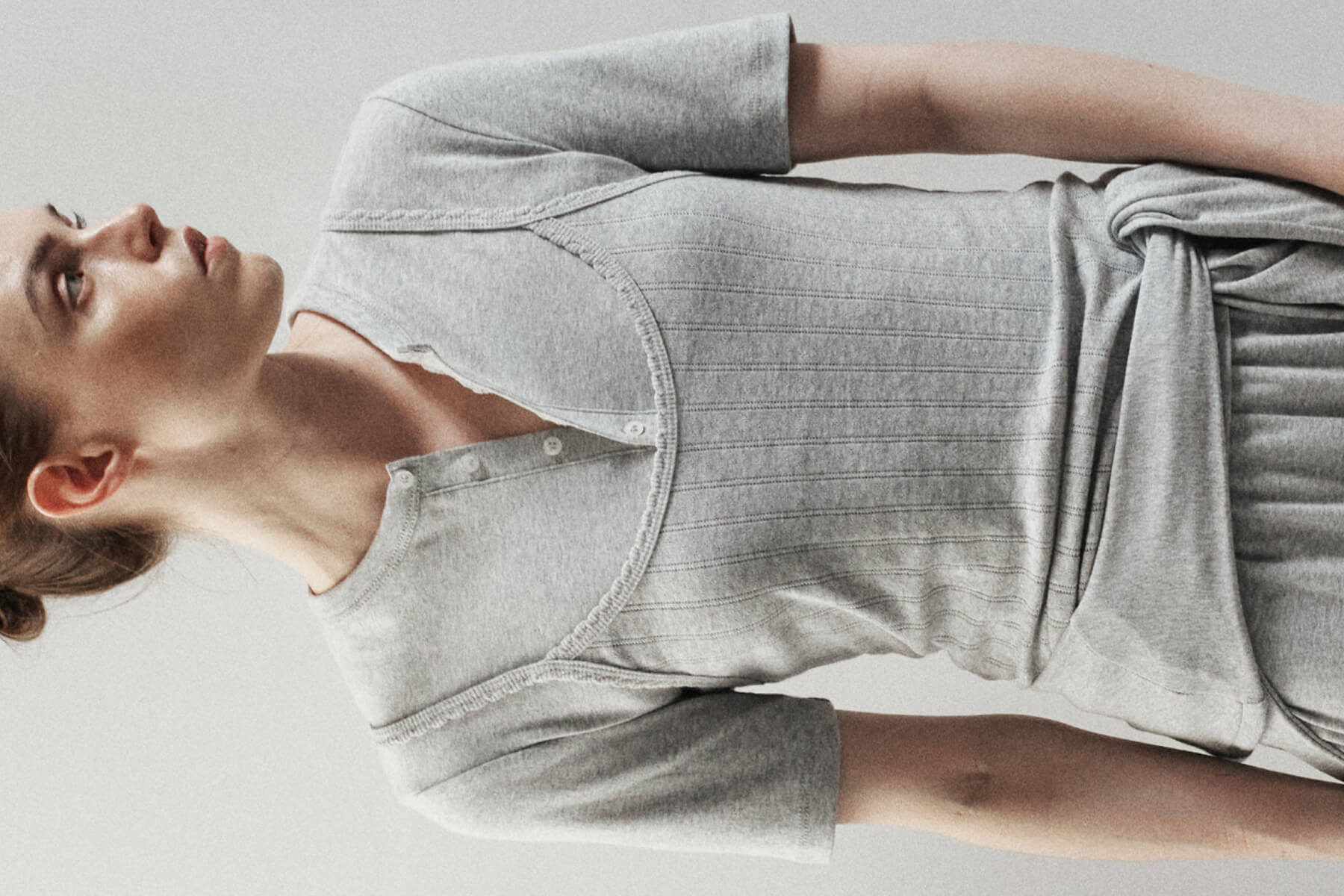 Side view of woman wearing layered grey tank over henley, looking to the side.