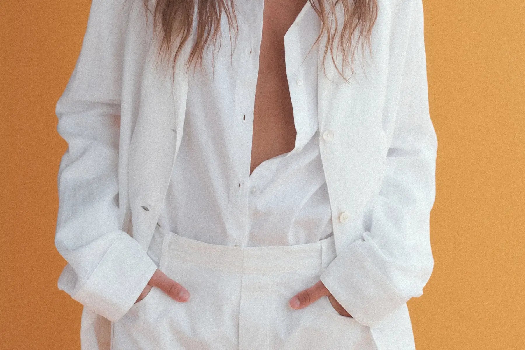 Close up of white button down, with white blazer layered over, tucked into white pants.