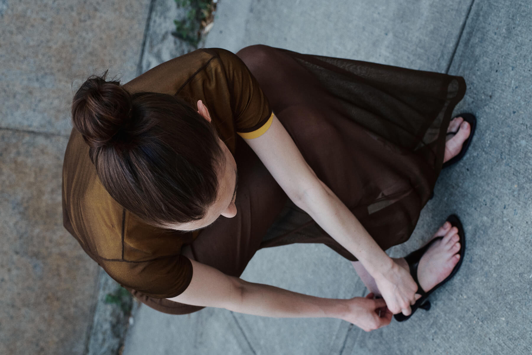 Woman kneeling down in brown top and skirt with sandals outside