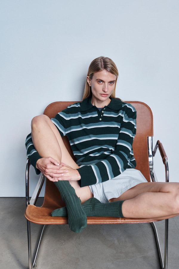 Woman in James striped polo sweater with shorts and green socks, sitting in chair