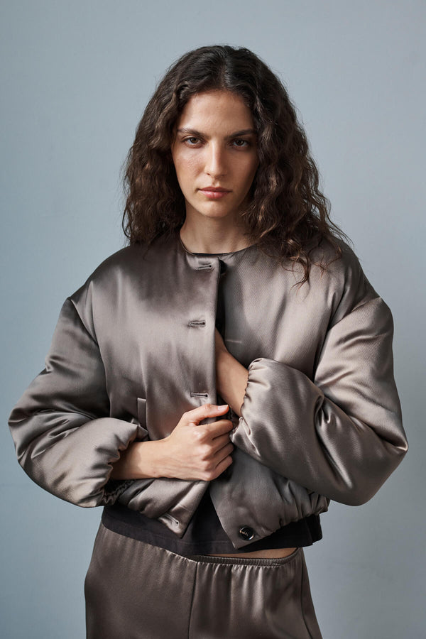Woman looking off into distance, holding here barb bomber satin taupe jacket