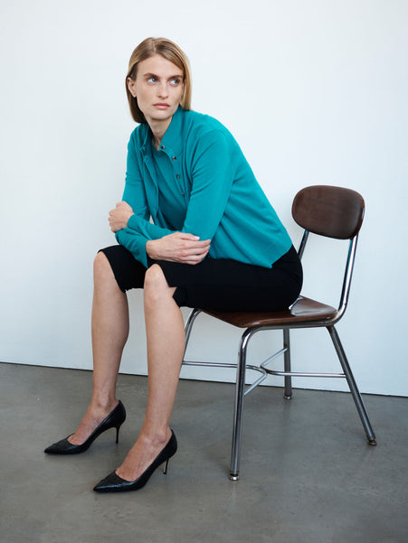 Woman sitting in chair in James Caribbean sweater set, rio black capri pants and heels