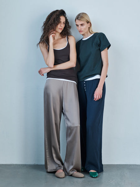 Two women standing against a wall in Pointelle tanks, Barb pant in taupe, and Margo tee forest layered over white with Pointelle boxer pants.
