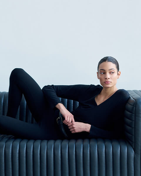 Woman laying down on couch in black long sleeve tee and leggings with belt, looking to the side.