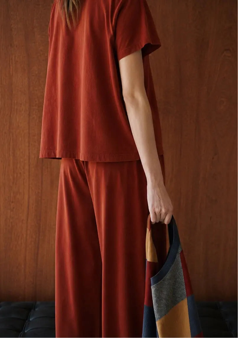 Back of model wearing rust colored tshirt and pants holding sweater
