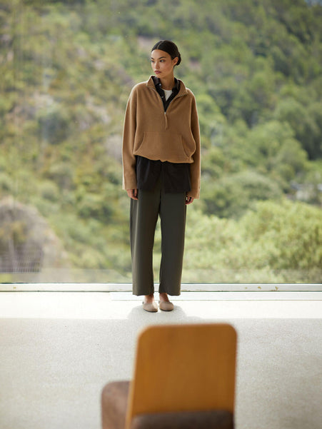 Woman standing by window with scenic view in Jess anorak camel and Chloe olive pants