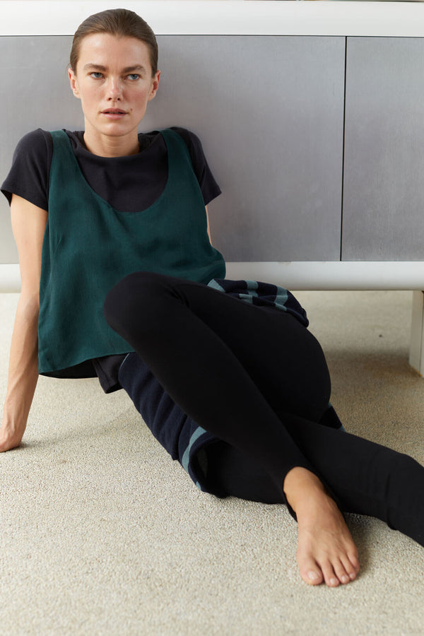 Woman in Kim spruce tank sitting on floor and black stirrup leggings