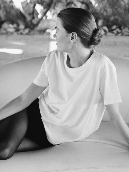 Woman in white t-shirt and tights sitting on couch outside