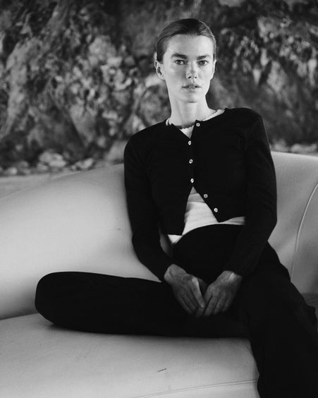 Woman sitting on couch outside in black cardigan and pants