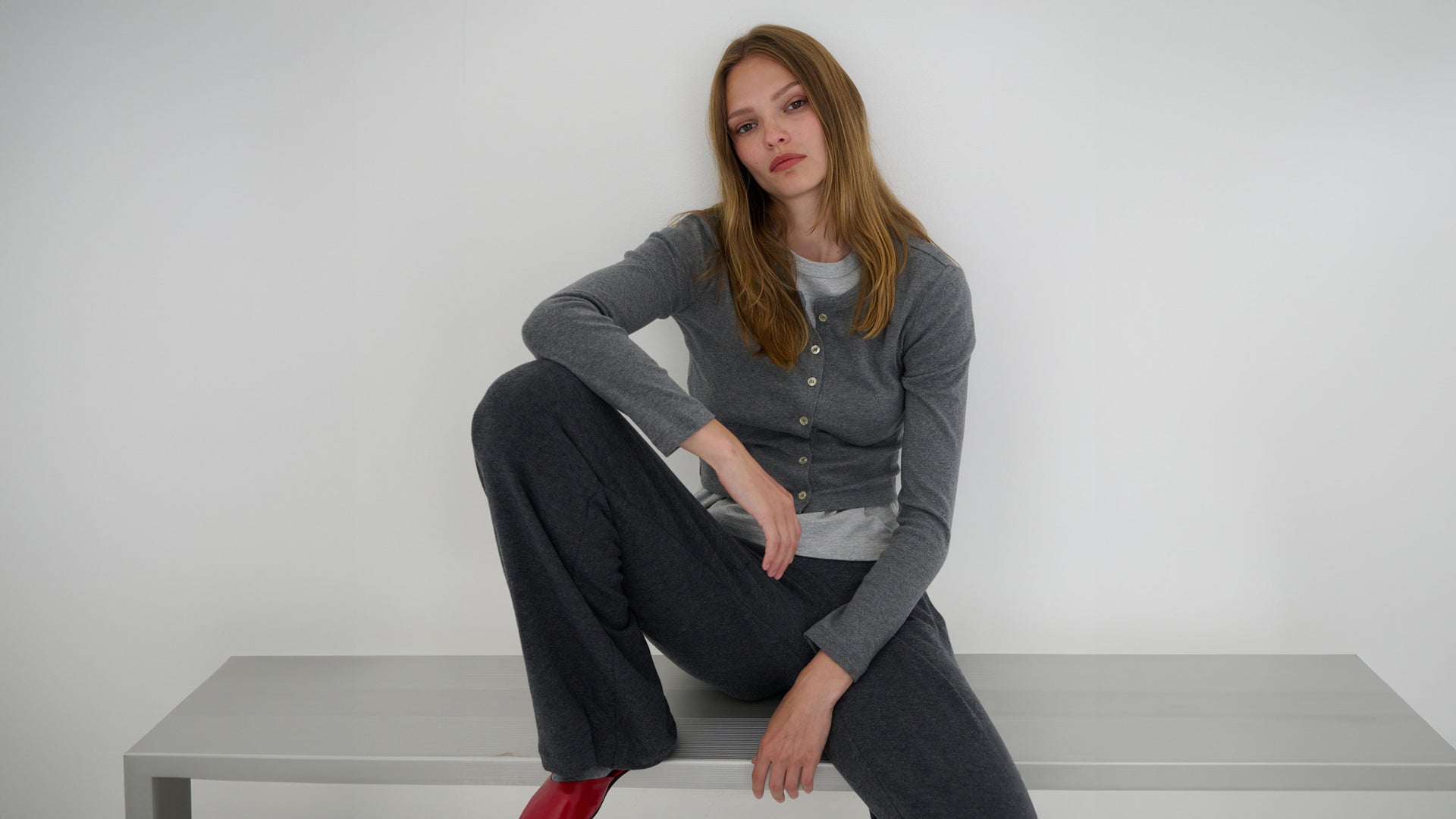 Woman sitting on bench in Granite nando and pants and sweater, and heather grey Margo, with Ruby red Romy mules.