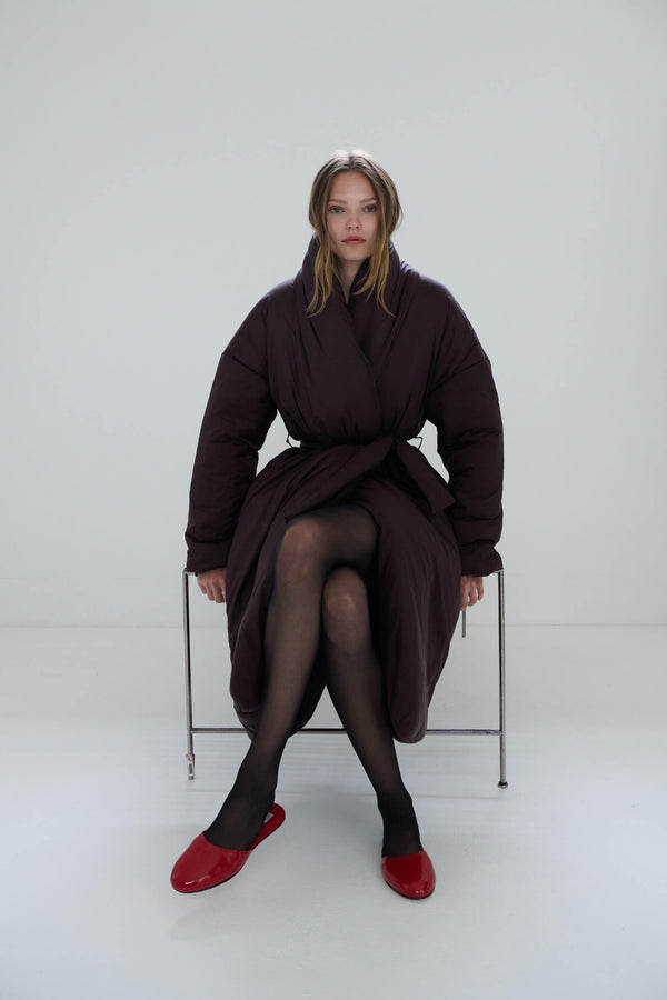 Woman sitting down in Bo shawl puffer coat and ruby red Romy mules.