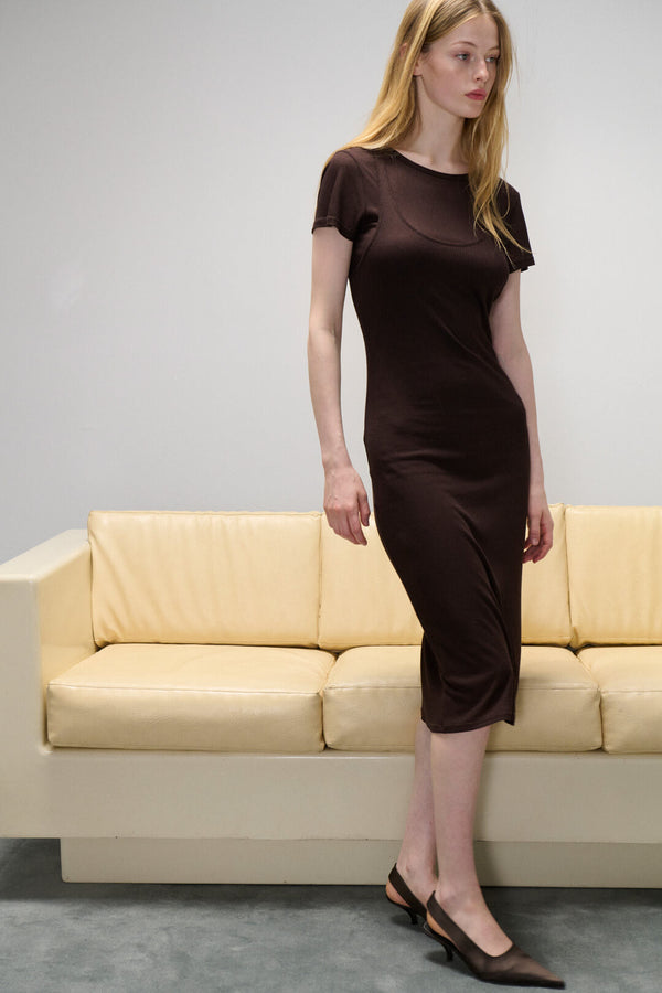 Woman standing in Rozzi choco dress in front of yellow couch.