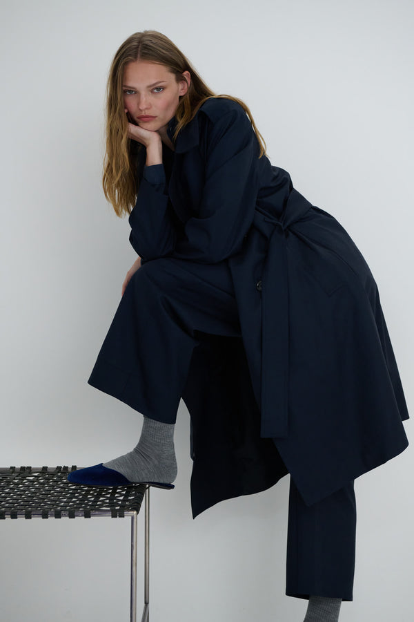 Woman standing and leaning with one foot on stool, in Jane navy coat and socks.