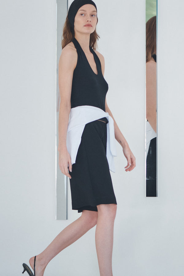 Woman walking in black shorts and black halter top, with cardigan wrapped around waist.