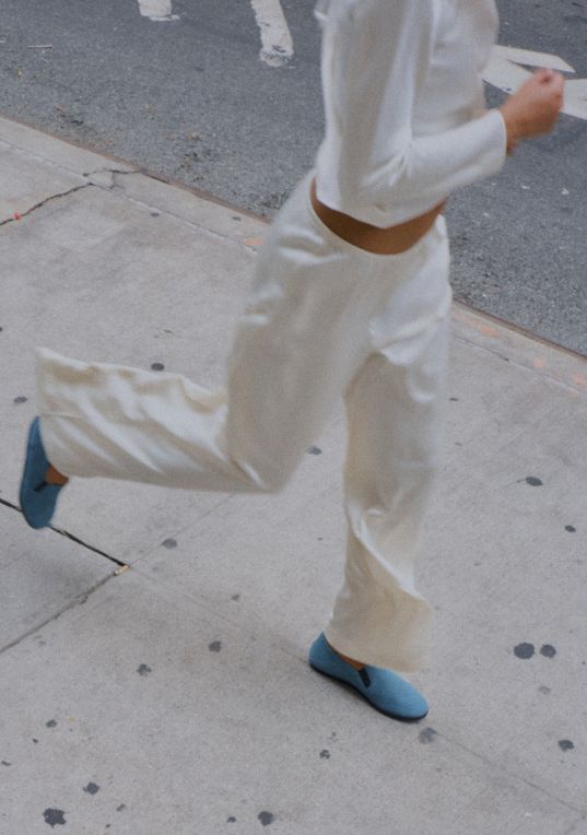 Model is running in blue sueded loafers and satin creme pants