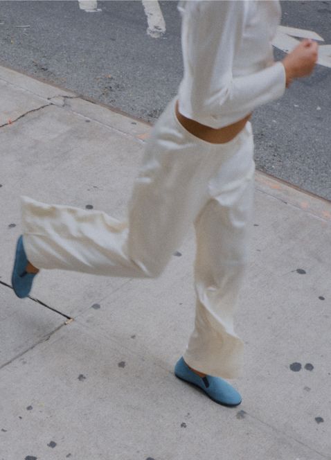 Model is running in blue sueded loafers and satin creme pants