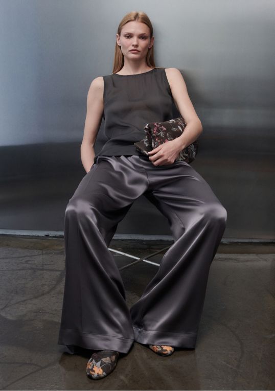 Model is leaning down barb satin wide leg in gunmetal and farrah sleeveless top.