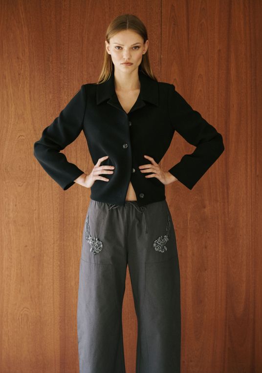 Model is standing with arms crossed wearing embroidered kyoto pants and black jacket.
