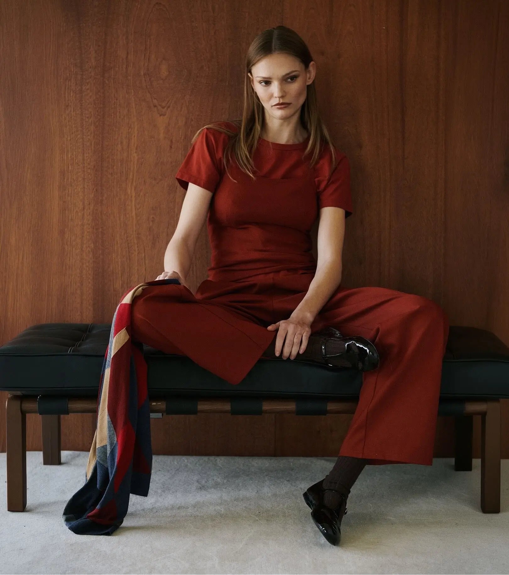 Model is sitting wearing red matching tshirt and pants, holding argyle sweater