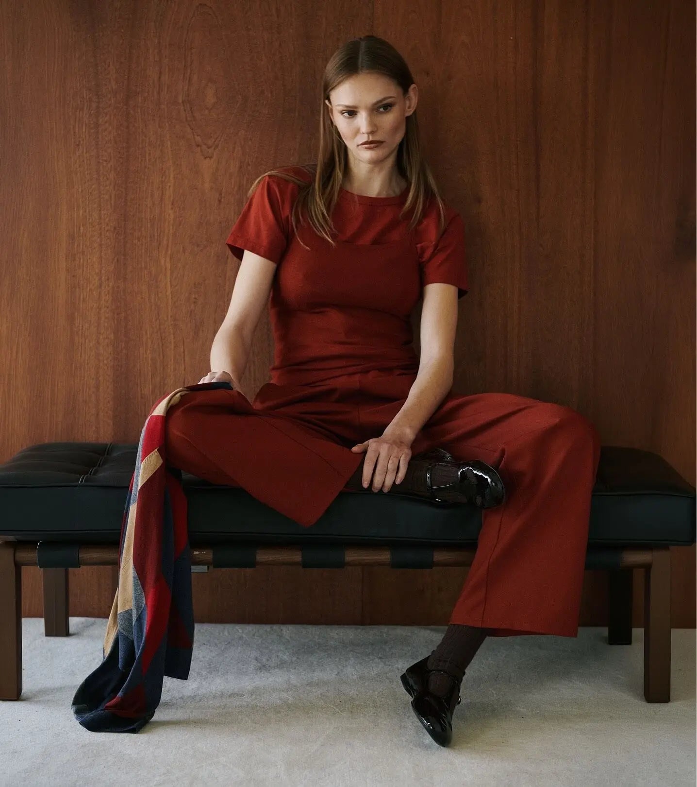 Model is sitting wearing red matching tshirt and pants, holding argyle sweater