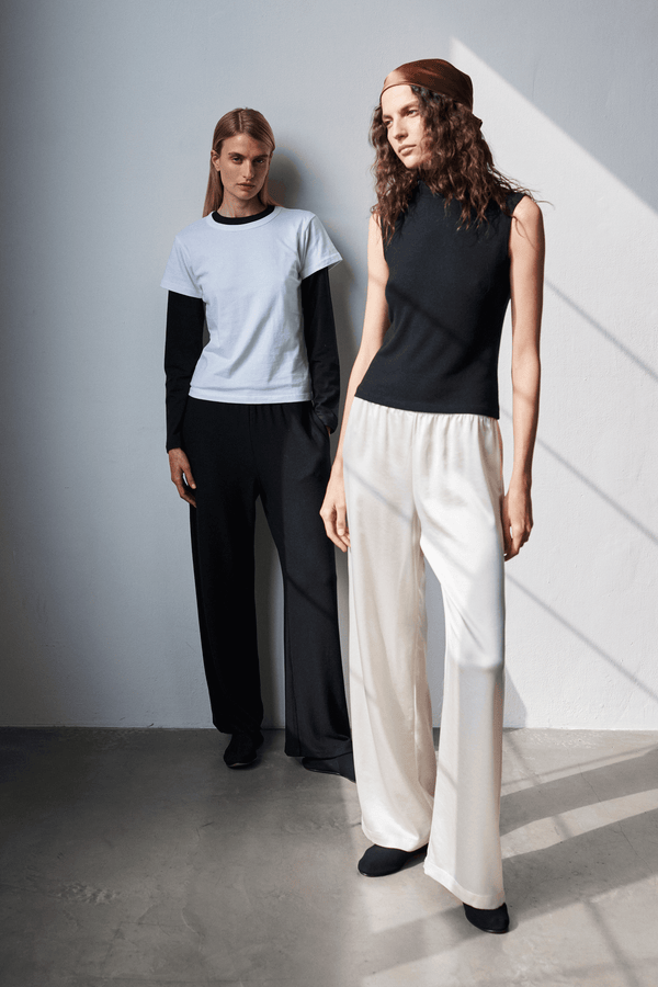 Two women standing against blank wall in layered tshirt, Barb satin pants.