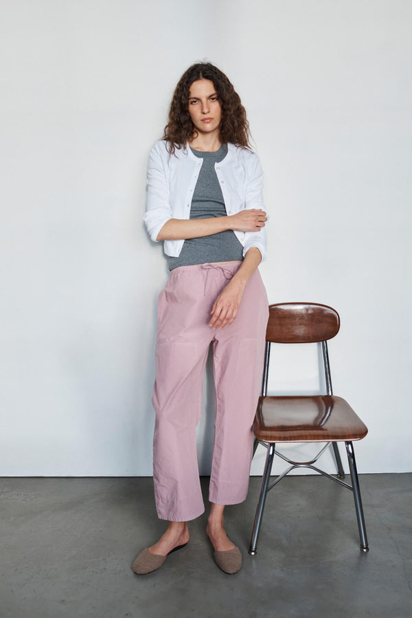 Woman standing in Kyoto maud carpenter pants by chair, in a cardigan looking off into distance