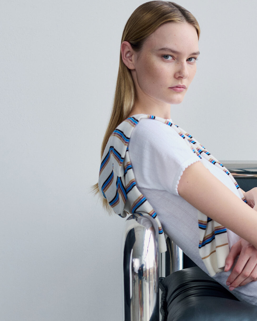 Woman sitting back on side of chair in white Pointelle tee and James striped sweater draped over.