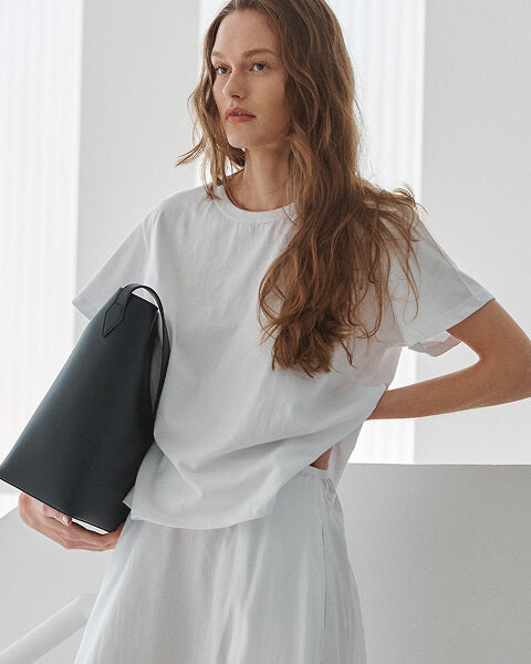 Woman wearing the white Margo t-shirt holding bag, with white skirt.