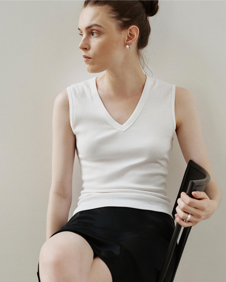 Woman sitting in white v neck tank and skirt looking to the side.
