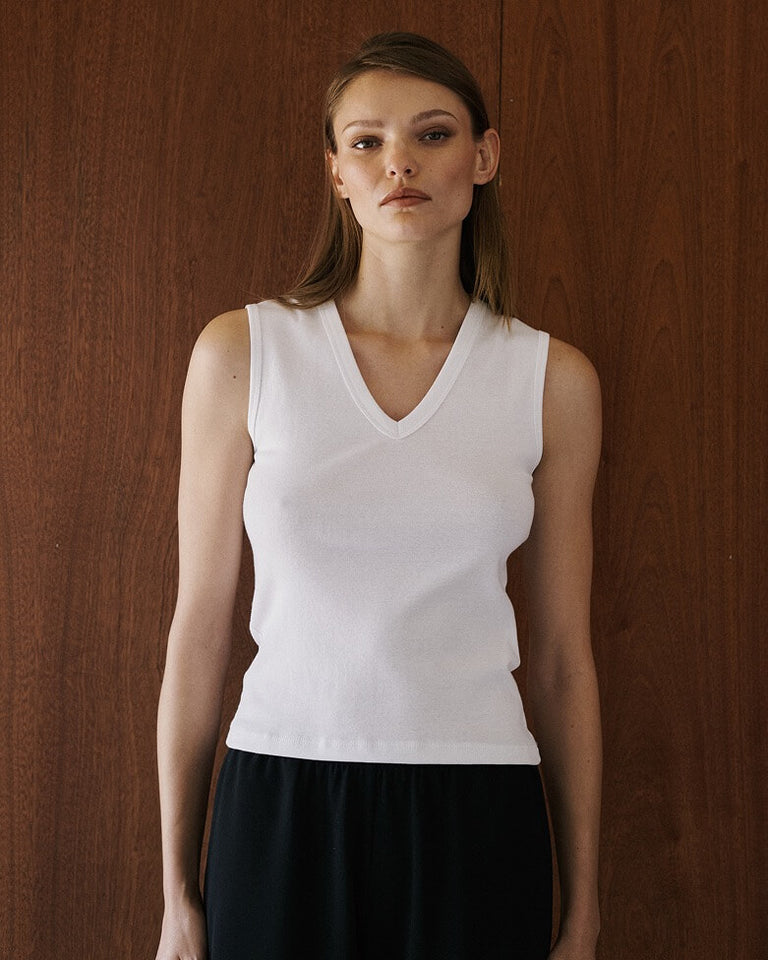 Woman wearing sleeveless white tank in front of wooden wall