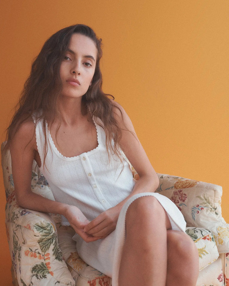 Woman sitting in floral chair in white Pointelle with orange background.
