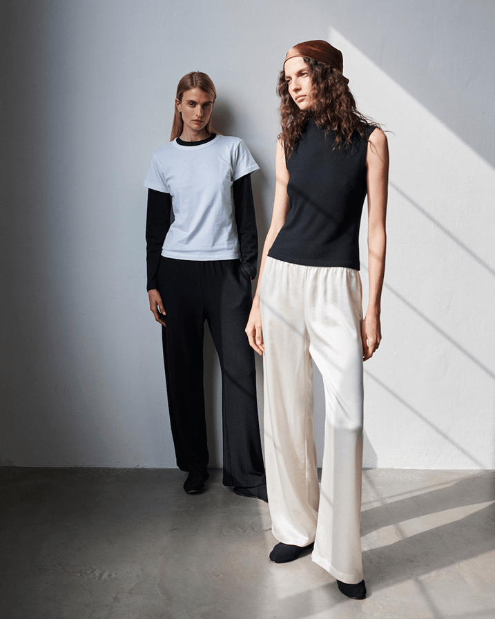 Woman in Kyoto maud carpenter pants and granite tshirt, with layered cardigan standing next to a brown chair.