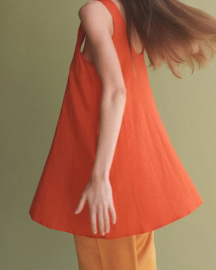 Woman sitting down in floral chair with orange background, wearing white Pointelle button down tank.