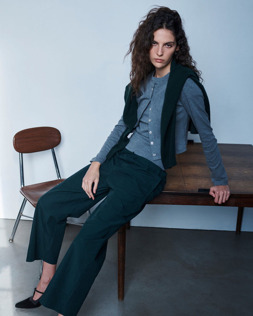Woman leaning against wooden table in forest Kyoto pants and granite nando cardigan set.