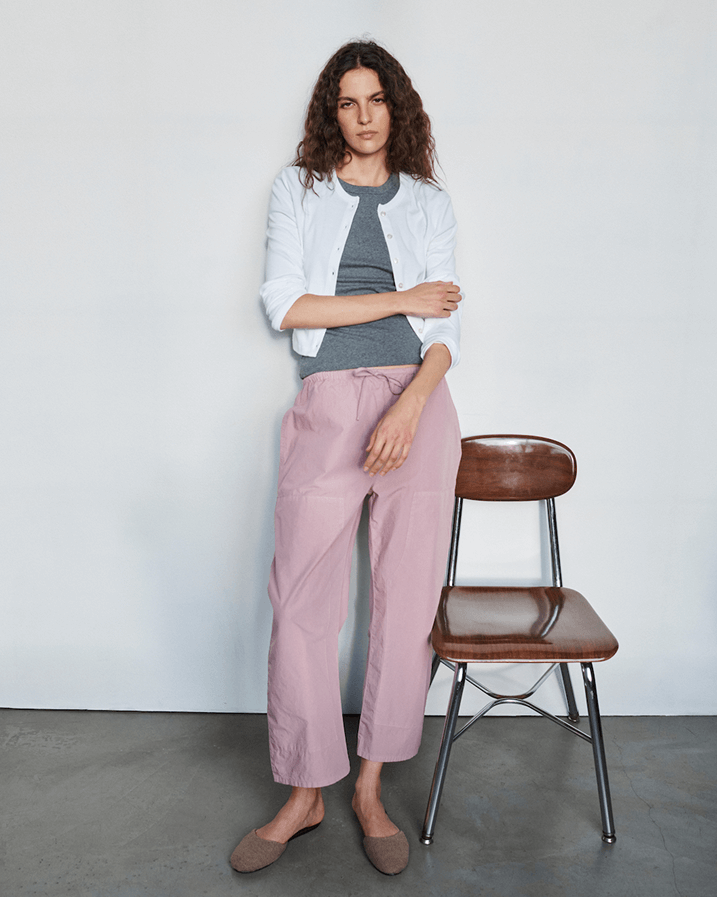 Woman in Kyoto maud carpenter pants and granite tshirt, with layered cardigan standing next to a brown chair.