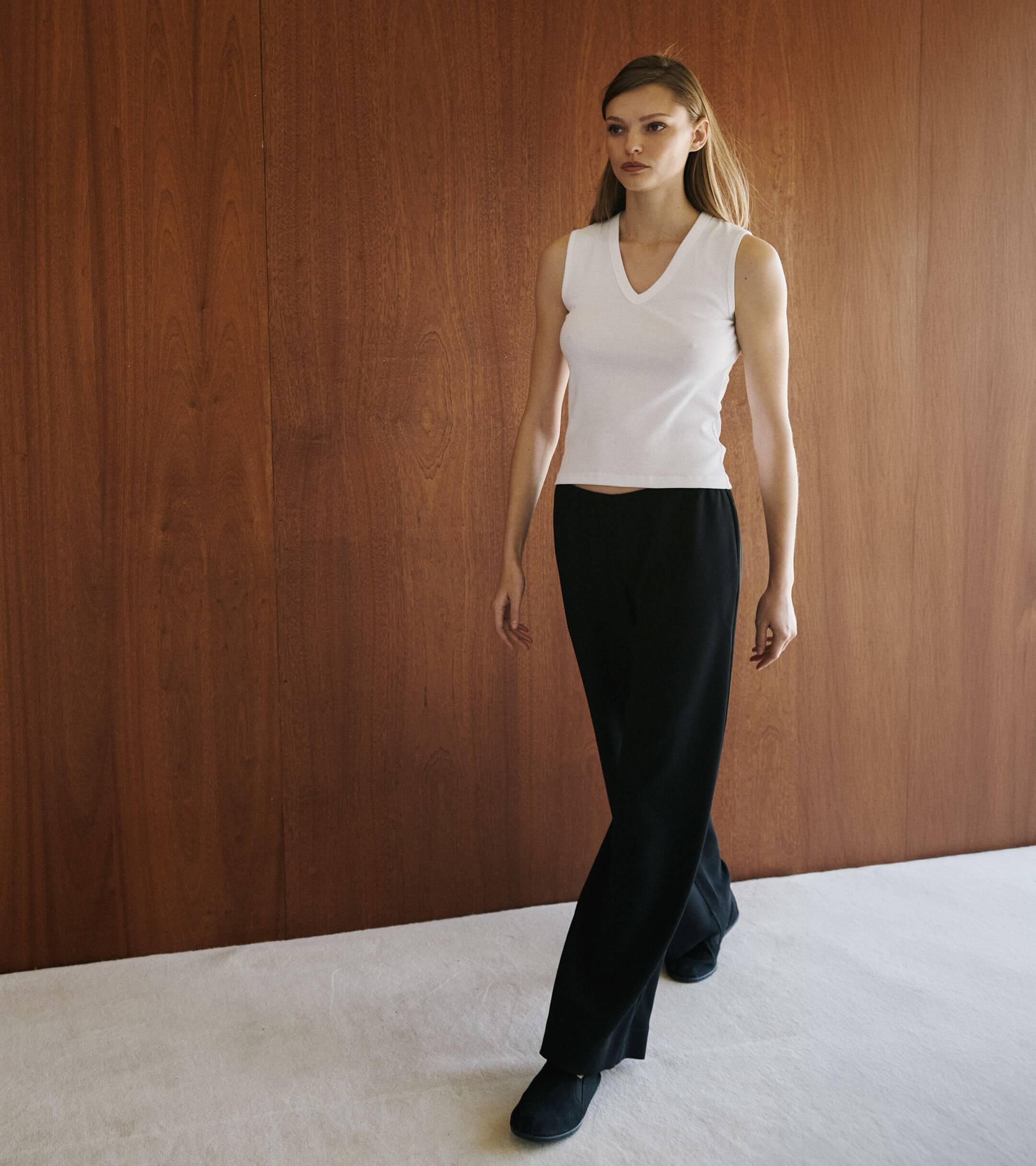 Woman walking in white sleeveless cotton tank and black skirt.