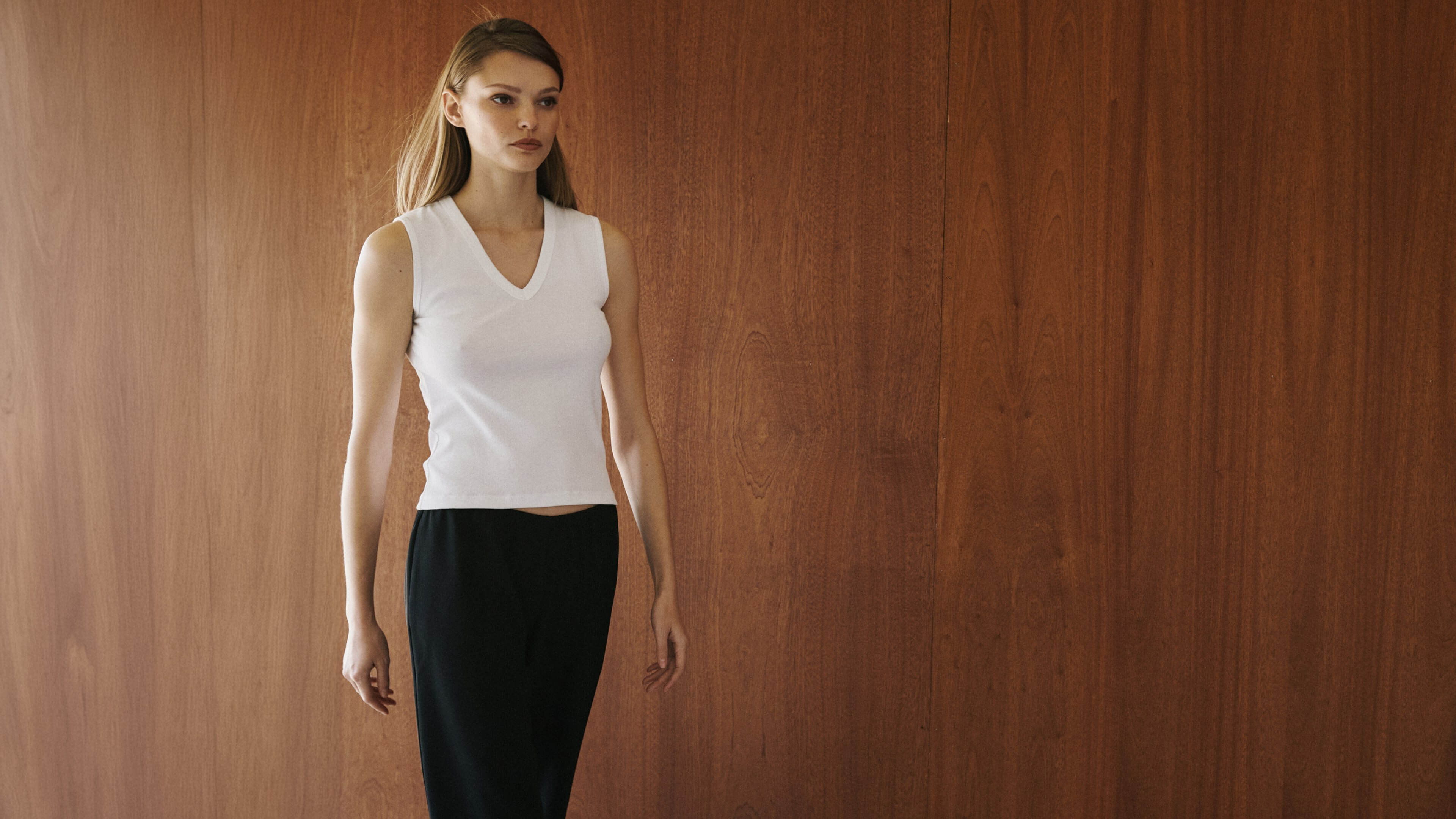 Woman walking in white sleeveless cotton tank and black skirt.