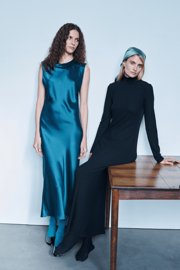 Two woman leaning against table in maxi dresses, pacific blue satin and black Lauren.