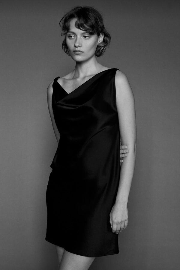 Woman standing against wall in Black Barb dress, in black and white