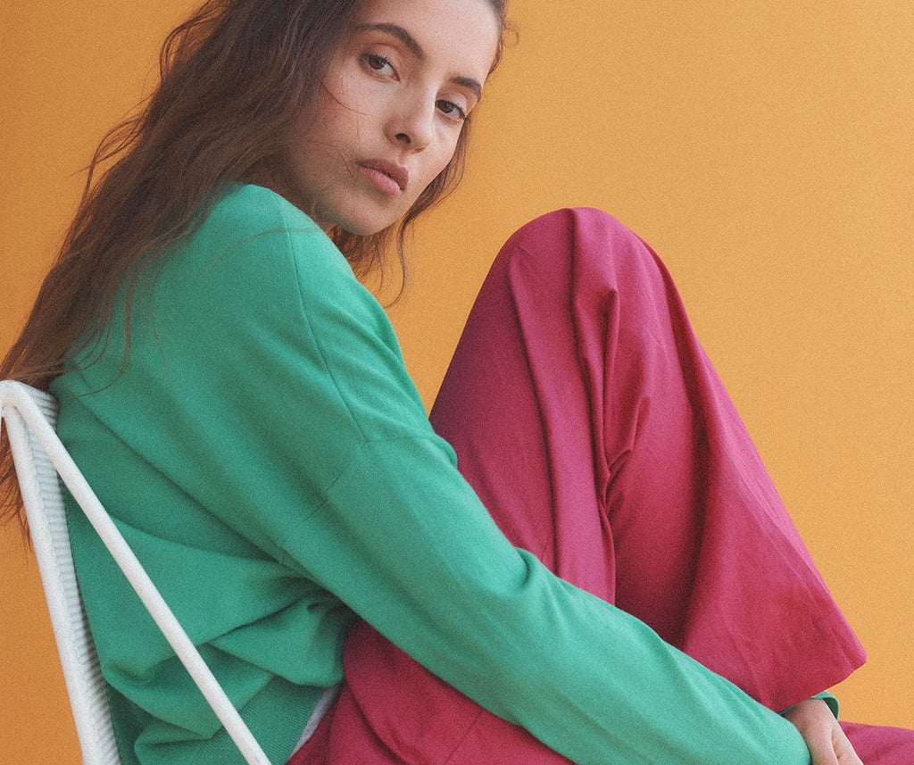 Close up of woman sitting in chair in green oversized sweater and pink carpenter pants.