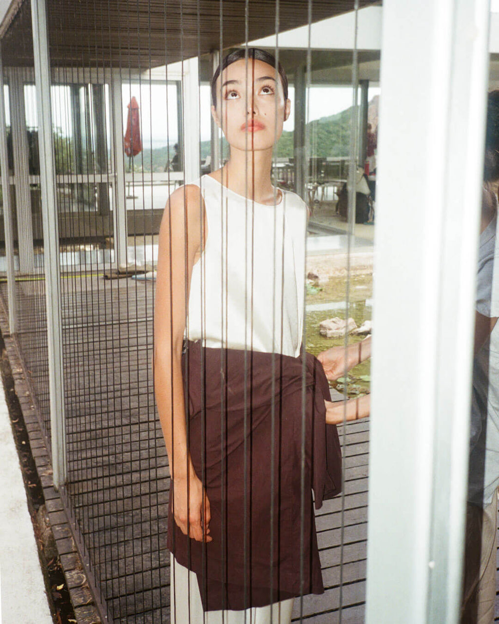 Woman looking through window in satin creme set with brown sweater tied around waist