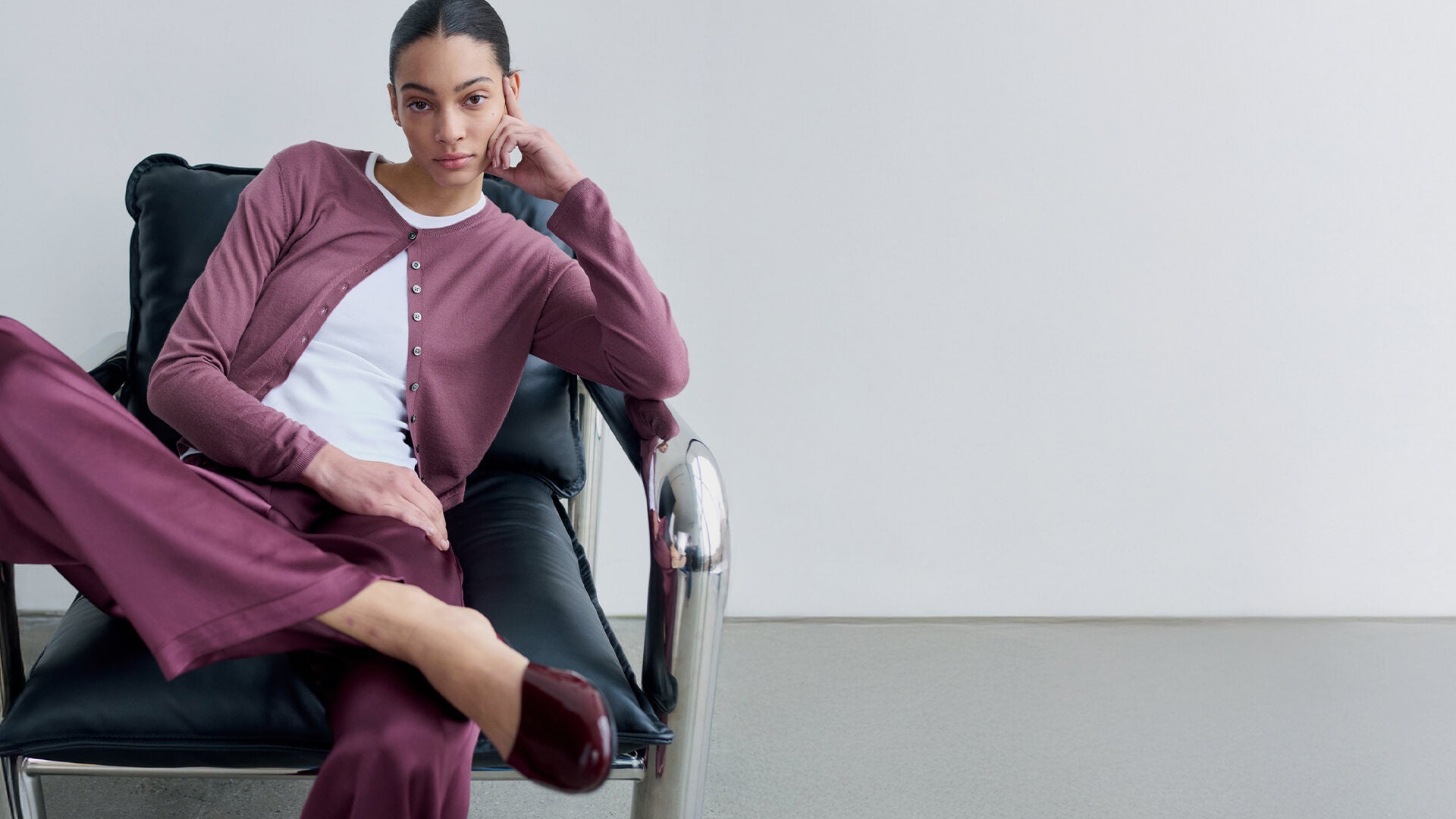 Woman sitting in chair in James dusty rose and satin pants, with Romy mules looking straight ahead.