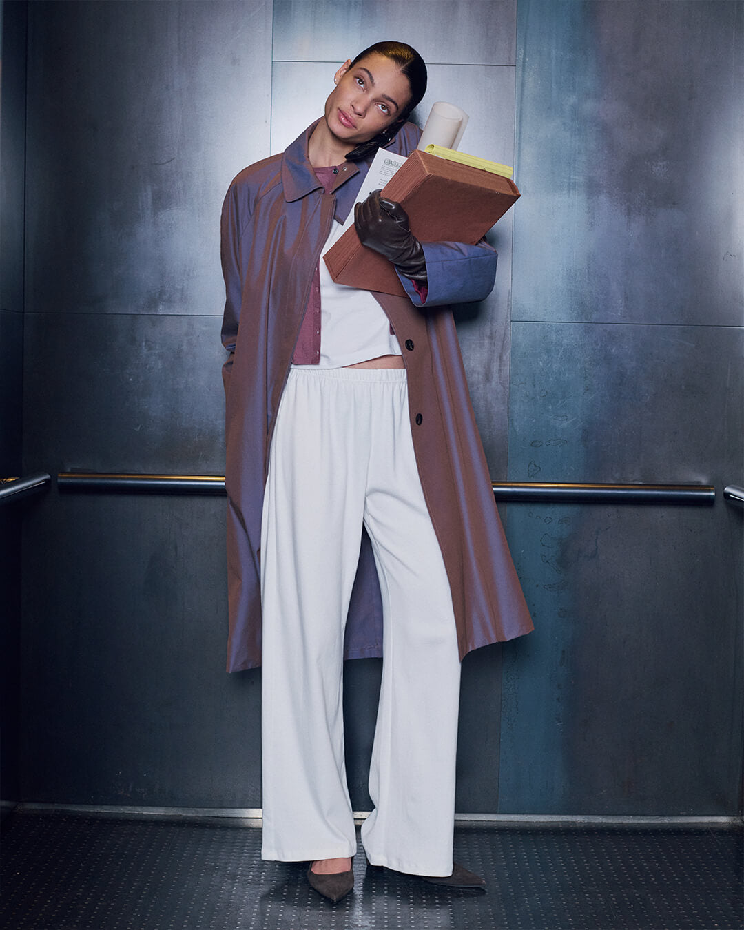 Woman standing in white Nando sweat set with Yuki rosewood colored car coat, on phone holding books with gloves.