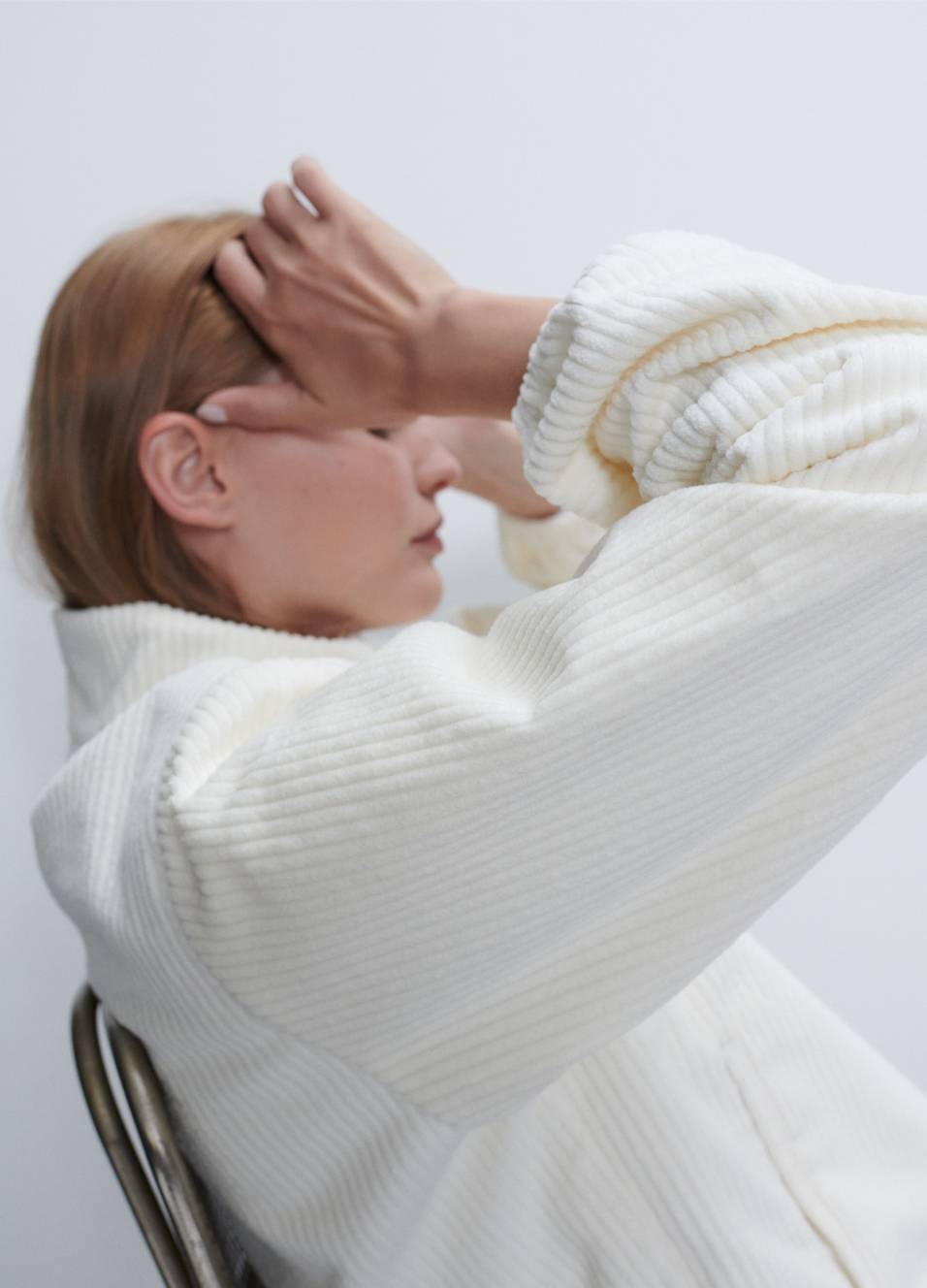 Model is sitting in metal chair facing the side wearing sammi corduroy white jacket.