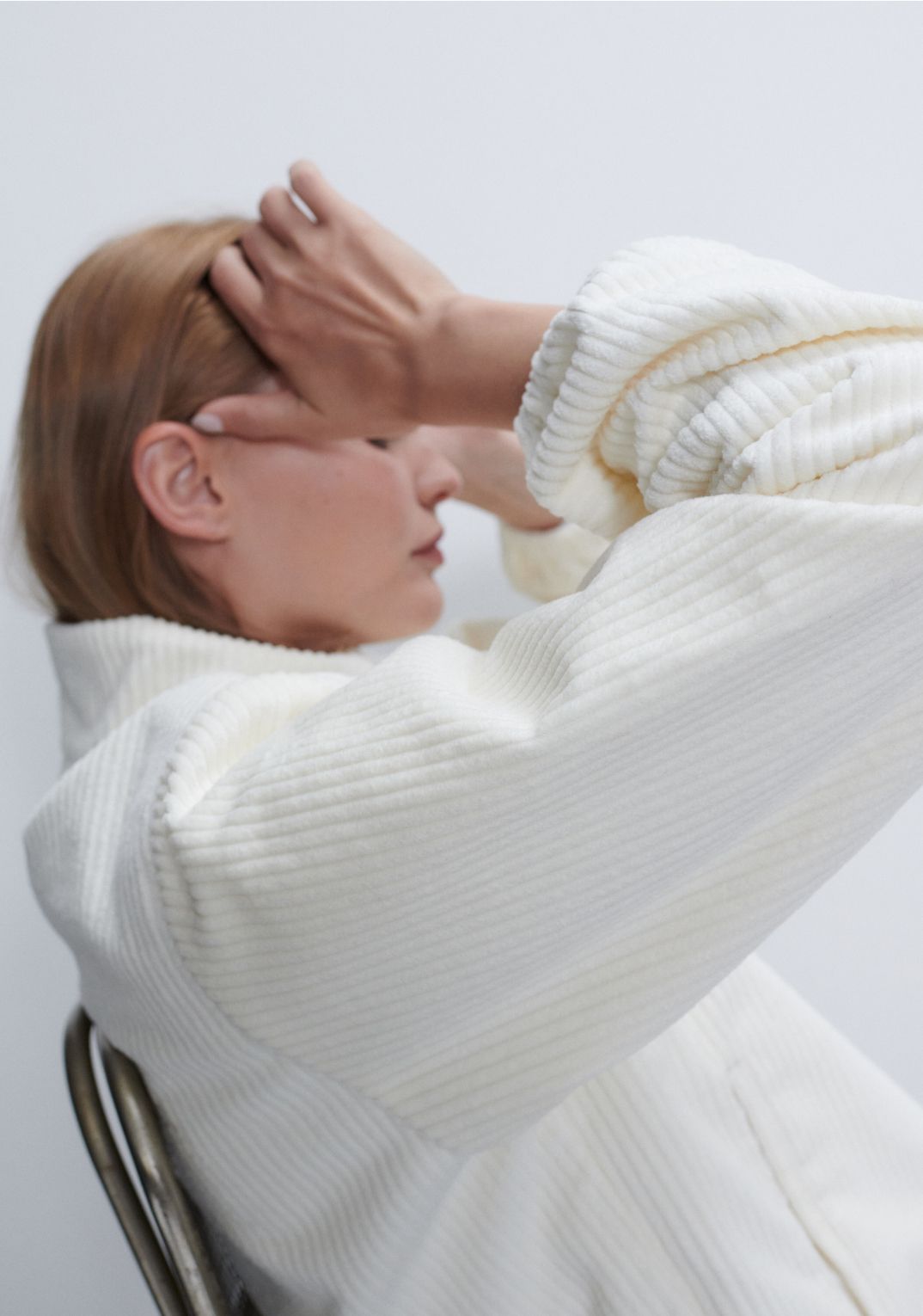 Model is sitting in metal chair facing the side wearing sammi corduroy white jacket.