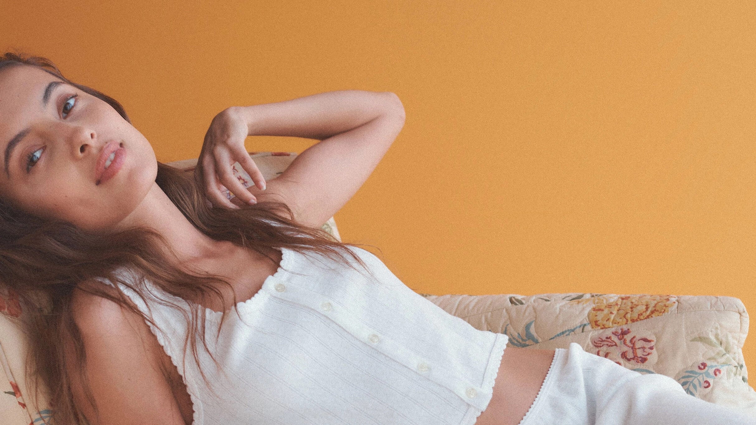 Woman leaning down in Pointelle white top with orange background.